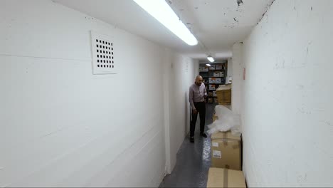 Asian-Indian-Male-walking-towards-camera-in-corridor-looking-through-boxes