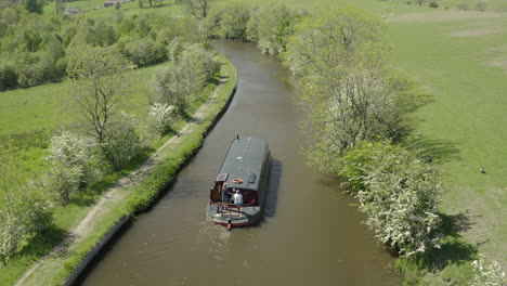 An-aerial-view-of-a-canal-boat-traveling-down-a-canal-surrounded-by-Yorkshire-countryside-on-a-sunny-spring-day