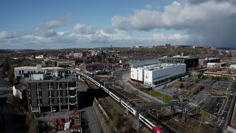 Aerial-footage-of-trains-approaching-Stoke-on-Trent-train-station-in-the-midlands-by-the-canal,-waterside-and-A50-motorway