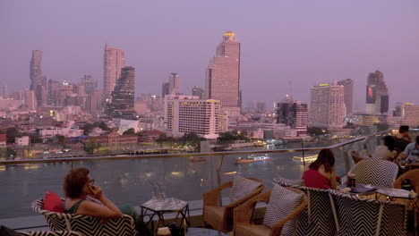 Turistas-Sentados-En-La-Plataforma-De-Observación-Con-Bebidas-Mirando-Vistas-Panorámicas-A-Través-Del-Horizonte-De-La-Ciudad-De-Bangkok