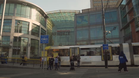 4K-entrance-to-Manchester-Arndale-centre-with-Metrolink-tram-passing-left-to-right-with-people-walking-in-view