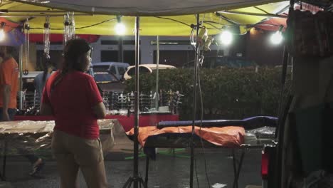 Es-Regnet-Auf-Dem-Nachtmarkt,-Während-Menschen-Mit-Regenschirm-Am-Straßenhändlerstand-Vorbeigehen