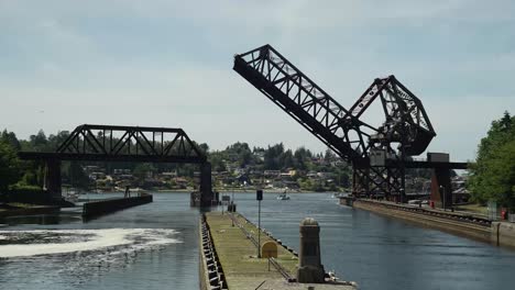 Time-Lapse-of-boats-exiting-and-entering-the-Ballard-Locks,-train-trestle-opens-in-the-background