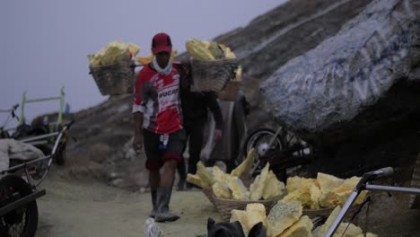 Kawah-Ijen-Schwefelarbeiter-Kommen-Am-Frühen-Morgen-Im-Hintergrund-Mit-Einem-Anhänger-Voller-Schwefel-Im-Vordergrund