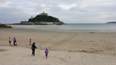 Madres-Y-Sus-Hijos-Caminando-En-La-Playa-De-Marazion-Frente-Al-Castillo-Medieval-Inglés-Y-La-Iglesia-Del-Monte-De-San-Miguel-En-Cornualles-En-Un-Día-Nublado-De-Primavera,-Imágenes-De-4k