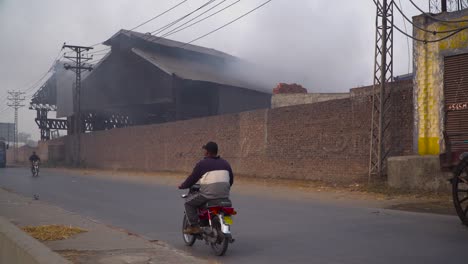 Panning-to-the-Industrial-pollution-that-is-effecting-the-population,-Traffic-is-going-on-with-the-factory,-Electric-polls-and-cables-at-the-road