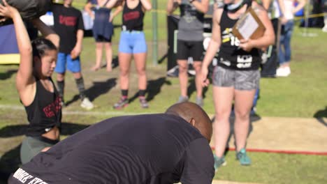 A-young-fit-athletic-black-male-struggles-doing-weighted-lifts-with-a-heavy-bag-together-as-a-team-during-a-cross-fit-competition-on-a-hot-sunny-day