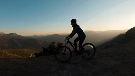 Girl-riding-her-bike-at-the-top-of-a-mountain-with-beautiful-canyon-lake-at-sunset-in-the-background