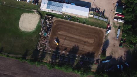 Aerial-directly-overhead-water-truck-wets-down-dirt-arena-in-an-effort-to-control-dust-from-the-horse-events-making-light-and-dark-pattern,-Kansas,-Missouri