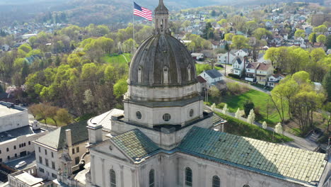 Aerial-drone-view-of-the-Cathedral-of-the-Blessed-Sacrament-in-Altoona,-Pennsylvania-with-the-American-flag-seen-behind