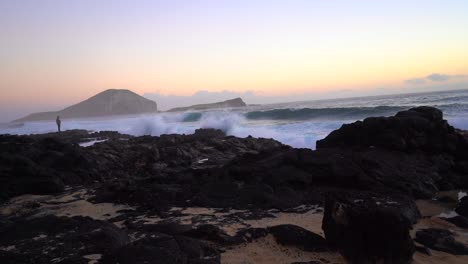 Flut-Rauscht-Bei-Sonnenaufgang-über-Die-Gezeitentümpel-Des-Makapuu-Strands,-In-Weiter-Ferne-Hält-Ein-Fotograf-Eine-Kamera-In-Der-Hand