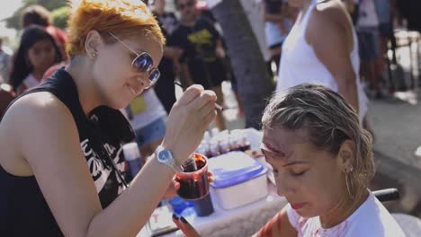 Make-up-artist-applying-products-painting-a-young-woman-in-a-wheelchair-before-Halloween-walk-of-zombies-on-the-Day-of-the-Dead-in-Copacabana