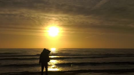 Silhouette-Eines-Mannes-Am-Strand,-Der-Den-Dunstigen-Sonnenaufgang-über-Dem-Ruhigen-Meer-Beobachtet