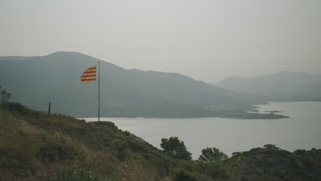 Die-Katalanische-Flagge-Weht-Im-Wind-In-El-Port-De-La-Selva-Und-Ein-Blick-Auf-Die-Berge-Im-Hintergrund