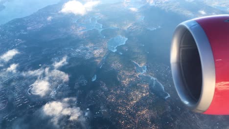 turbine-view-from-an-airplane-flying-above-the-clouds-and-a-city-near-the-sea-with-a-circular,-futuristic-building-in-Europe