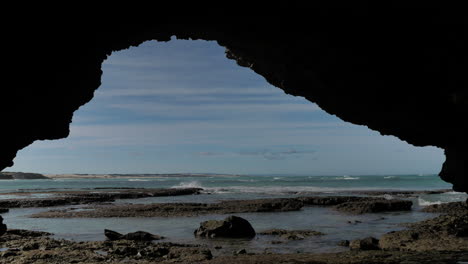 View-from-small-cave-on-rocky-coastline-of-waves-running-onto-shore,-static-shot