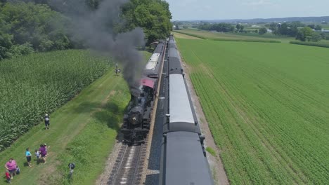 Aerial-View-of-a-1910-Steam-Engine-with-Passenger-Train-Puffing-Smoke-Traveling-Along-the-Amish-Countryside-as-a-Second-Steam-Train-Passes-on-a-Sunny-Summer-Day-as-Seen-by-a-Drone