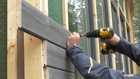 Worker-tightens-the-screw-with-a-screwdriver-on-house-wall-facade,-construction-work-concept