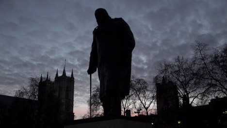 A-time-lapse-of-sunset-clouds-passing-a-silhouette-of-the-Winston-Churchill-in-Parliament-Square-and-Westminster-Abbey-in-the-background-with-planes-passing-overhead