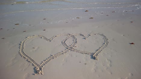 Turning-steadicam-shot-of-two-interlocking-hearts-inscribed-on-a-beach