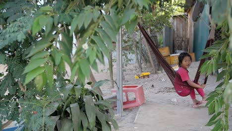 Small-girl-swinging-in-hammock-alone-suspended-in-rural-Laos-poverty-simple-garden,-comfortable---relaxing