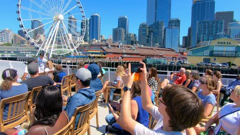 People-on-a-tourist-boat-sailing-by-the-Luna-park-with-panoramic-wheel-and-building-in-Seattle-at-the-back