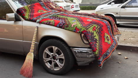 Parked-car-draped-with-colourful-handmade-rug-on-street-in-Yerevan,-Armenia