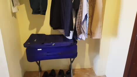 View-of-the-interior-of-a-small-hotel-closet,-with-shirts-and-a-suitcase