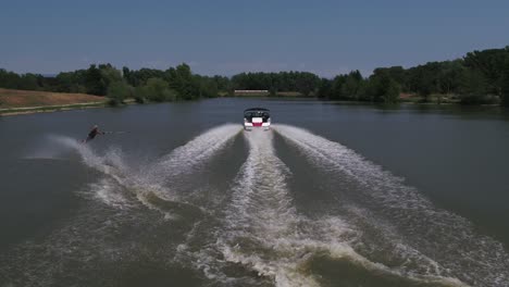 Person-slaloms-with-water-ski-pulled-by-a-speedboat,-tracking-shot