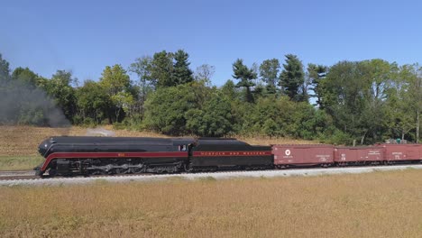 Luftaufnahme-Einer-Antiken-Dampflokomotive,-Die-An-Einem-Sonnigen-Herbsttag-Mit-Güterwaggons-Am-Bahnhof-Durch-Amisches-Ackerland-Angehalten-Hat,-Mit-Blick-Auf-Das-Wegfahren,-Gesehen-Von-Einer-Drohne