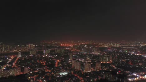 descending-drone-over-residential-area-of-major-Southeast-Asian-city-at-night-showing-sprawl,-high-rise-buildings,-major-roads-and-earlier-colonial-buildings