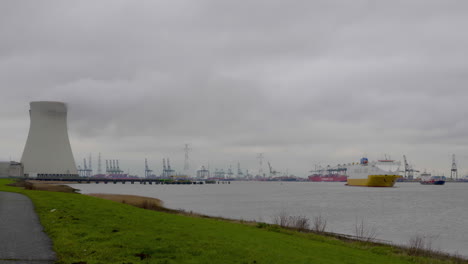 The-Antwerp-Harbor-in-Belgium-on-a-cloudy-day-with-shipping-barges,-boats-and-a-nuclear-power-plant-in-the-distance---Wide-shot