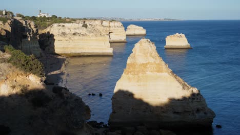 Establishing-shot,-People-Enjoying-the-sandy-coastline-in-rock-tunnel-beach-in-Algarve,-Portugal,-Sun-shading-the-coastline-in-the-background