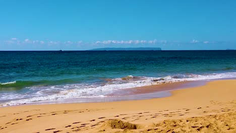 HD-Hawaii-Kauai-slow-motion-static-wide-shot-of-four-boats-in-a-line-going-from-right-to-left-with-an-island-in-background-and-waves-washing-up-on-the-beach-with-a-few-clouds-on-the-horizon
