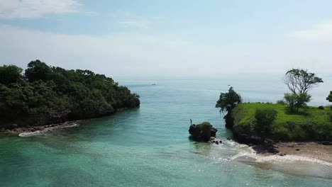 A-young-man-is-standing-on-the-edge-of-a-small-cliff,-looking-down-in-the-crystal-clear-water-on-a-tiny-islet-outside-Lombok,-Indonesia