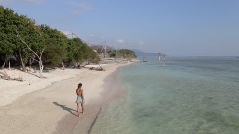 Woman-in-bikini-walking-on-lonely-beach-with-crystal-clear-ocean-water-on-Gili-Trawangan
