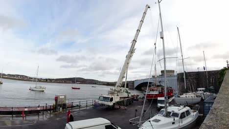 Hydraulic-crane-vehicle-lifting-heavy-fishing-boat-vessel-into-Conwy-harbour-waterfront-timelapse