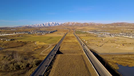 Volando-Por-Encima-De-Una-Carretera-Separada-Con-Tráfico-Ligero-En-Otoño-Con-Montañas-Nevadas-En-El-Fondo