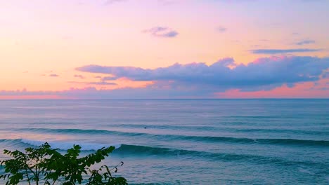 HD-Hawaii-Kauai-slow-motion-wide-shot-pan-from-right-to-left-over-a-tree-of-the-ocean-with-a-surfer-very-tiny-on-screen-with-a-beautiful-partly-cloudy-sky-near-sunset