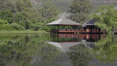 Reflection-of-mountain,-trees-and-Chinese-architecture-design-inspired-wine-tasting-building-with-patio-on-pond,-Stellenbosch