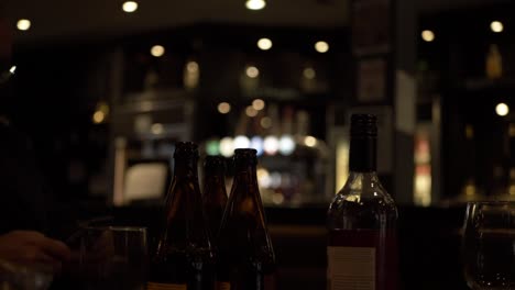 Waiter-in-bar-with-drinks-and-bottles-on-a-table-medium-panning-shot