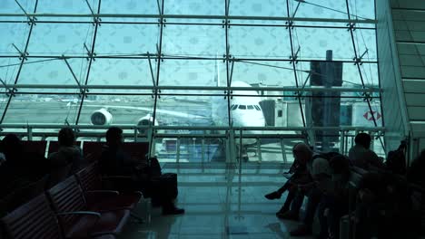 Flugzeug-An-Einem-Terminal-Im-Hintergrund,-Während-Menschen-Darauf-Warten,-Ihren-Flug-Zu-Erreichen,-Silhouettenaufnahme