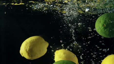 Close-up-of-falling-ripe-lemons-and-limes-into-sparkling-water-on-black-background,-making-cocktail-of-citrus,-drinking-cold-lemonade,-shooting-of-carbonated-water-with-floating-fruits-and-bubbles