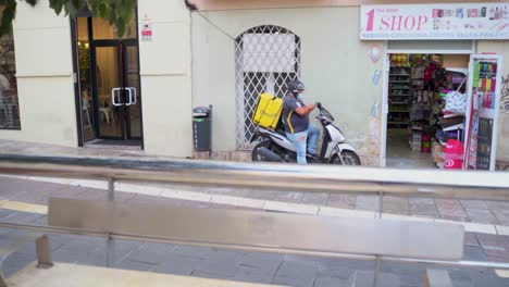 Lieferfahrer-Nutzt-Smartphone,-Während-Er-Auf-Seinem-Motorrad-Vor-Einem-Geschäft-An-Der-Straße-In-Der-Stadt-Málaga,-Spanien,-Sitzt-–-Ausbruch-Des-Coronavirus-–-Schuss-Nach-Vorne