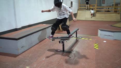 Junger-Skateboarder-Mit-Maske,-Der-Während-Des-Indoor-Skateboard-Trainings-Auf-Die-Schiene-Springt-Und-Schleift