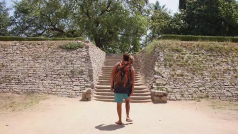Mochilero-Caminando-Hacia-Una-Escalera-Fuera-De-La-Ruina-De-Un-Templo-En-Hampi,-India---Toma-De-Reenvío