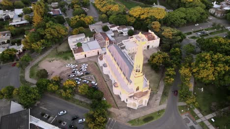 Aerial-lowering-beautiful-neo-gothic-church-surrounded-by-trees-in-the-middle-of-Santa-Elisa-countryside-town,-Entre-Rios,-Argentina