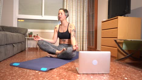 Woman-performs-yoga-breathing-and-greets-her-online-class-using-computer