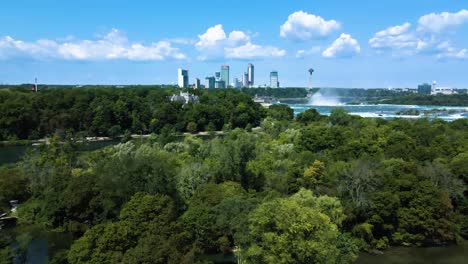 Aerial-backwards-shot-of-Niagara-Falls,-skyscraper-skyline-and-rural-forest-with-trees-on-canadian-border