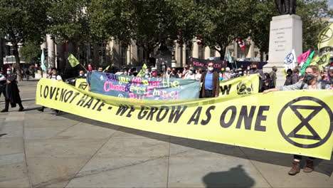 Auf-Dem-Trafalgar-Square-Versammeln-Sich-Demonstranten-Der-Rebellion-Gegen-Den-Klimawandel-Hinter-Einem-Gelben-Banner-Mit-Der-Aufschrift-„Liebe,-Nicht-Hass-–-Wir-Wachsen-Als-Einheit“.